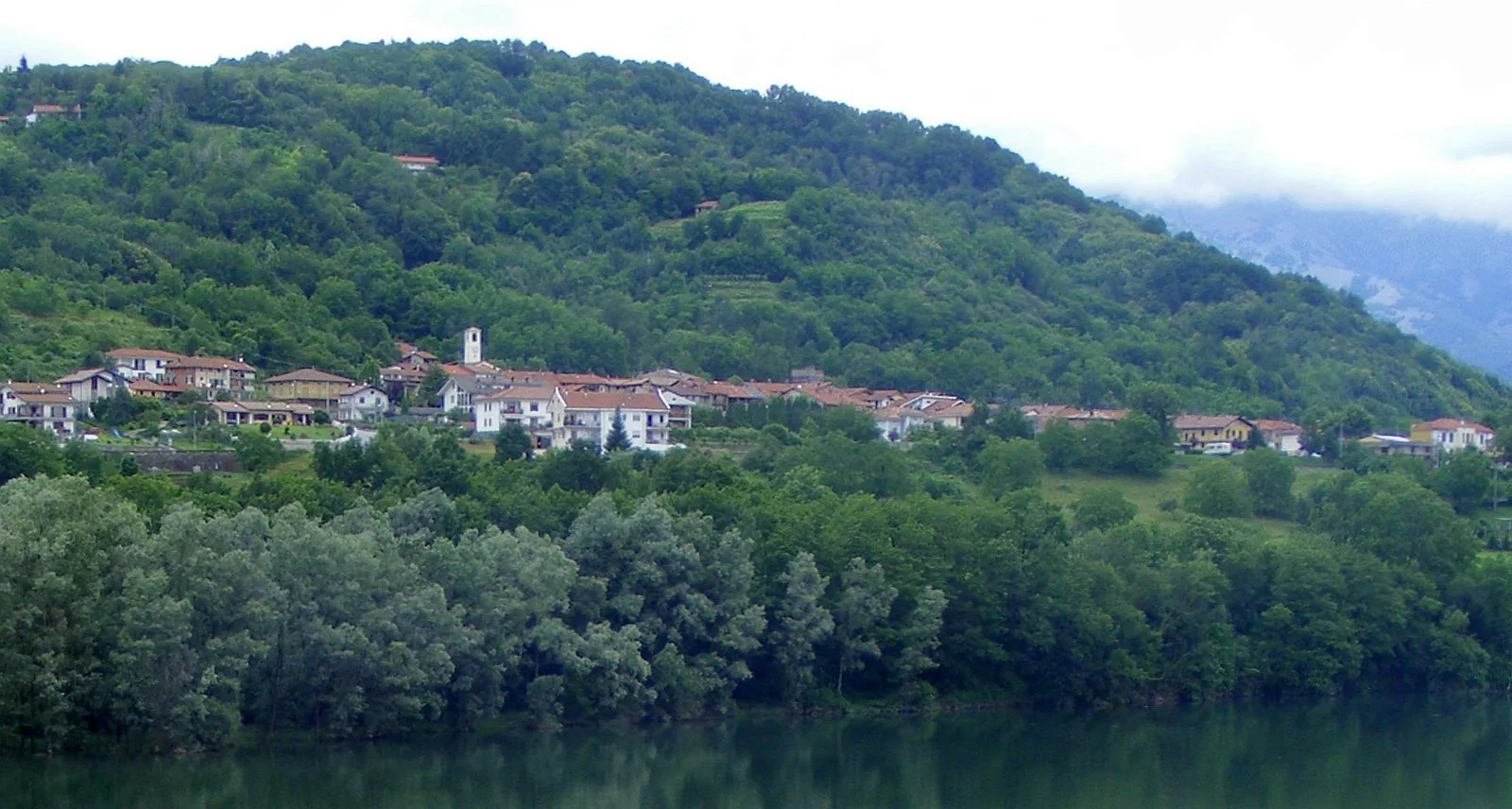 Il paese di Vidracco sulla collina boscosa, visto dalla sponda del lago di Gurzia